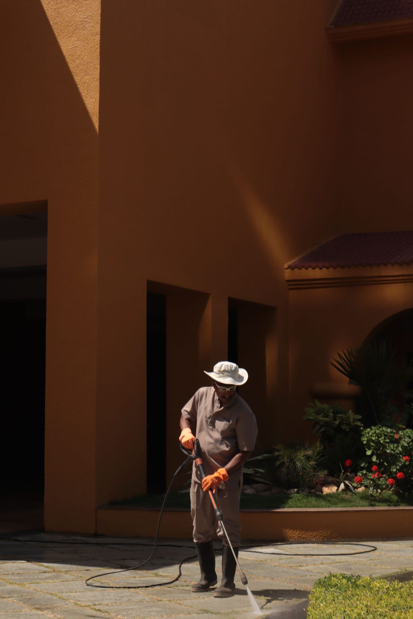 Worker pressure washing a paved walkway beside a stucco home